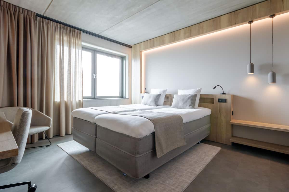A modern hotel room with a large bed, a desk, and a chair.