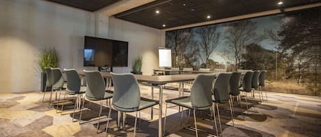 A conference room with a large table, multiple chairs, a flat-screen TV, and a projection screen.