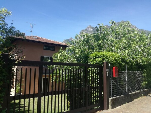 Una casa con patio cercado, buzón y montaña al fondo.
