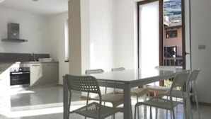 Une cuisine moderne avec des armoires blanches et un four encastré. On y trouve un coin repas avec une table blanche et quatre chaises.