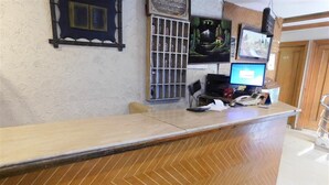 A reception desk with a wooden herringbone pattern, a computer monitor, a telephone, and a wall-mounted TV. - Hotel Al Noor (Lahore)