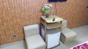 A room with a small desk, a television mounted on the wall, and two cushioned seating areas. - Hotel Al Noor (Lahore)