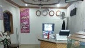 A reception area with a wooden counter, a computer monitor, and a wall-mounted clock. - Hotel Al Noor (Lahore)