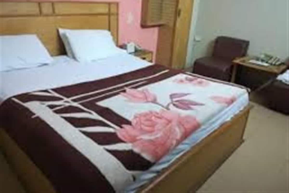 A hotel room with a bed, a chair, a nightstand, and a window with blinds.