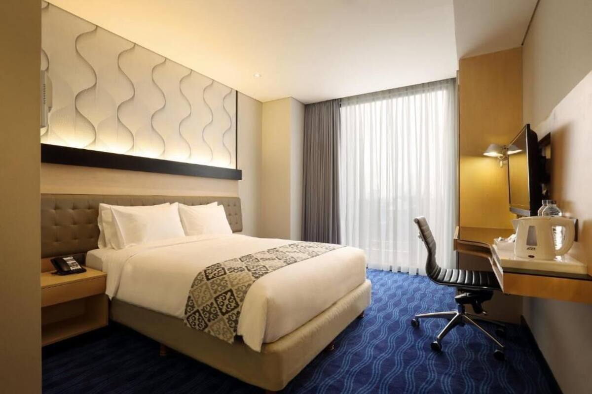 A hotel room with a large bed, a desk with a chair, a telephone, and a mirror.