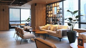 A modern lounge area with a sofa, chairs, a coffee table, and a bookshelf filled with books and decorative items. - AI HOTEL JAKARTA THAMRIN (Jakarta)