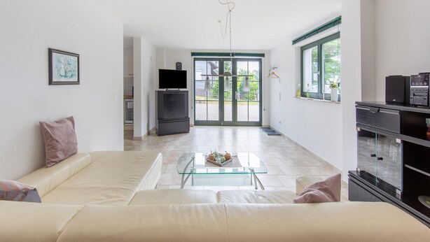 Una sala de estar moderna con un sofá, una mesa de centro de vidrio, un televisor y una cocina al fondo.