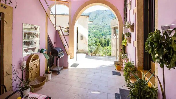 A cozy interior with a wooden ceiling, a view through an archway to a mountainous landscape, and a variety of potted plants. - Snug Apartment in Kournas With Balcony/terrace (Apokoronas)