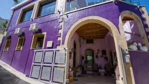 A two-story building with a purple facade, a balcony, and a covered entrance with a wooden ceiling. - Snug Apartment in Kournas With Balcony/terrace (Apokoronas)