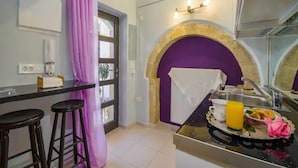 A kitchen with a purple arch, a bar area with stools, and a breakfast tray with orange juice. - Snug Apartment in Kournas With Balcony/terrace (Apokoronas)