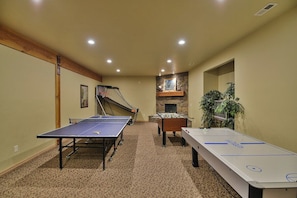 A room with a ping pong table, foosball table, and a foosball table with a stone fireplace in the background.