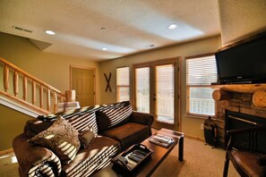 A living room with a brown leather sofa, a coffee table, a fireplace, a television, and a staircase.