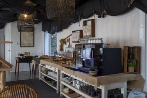 Un café chaleureux au décor rustique, avec une machine à café, des étagères remplies de tasses et un luminaire suspendu en osier.
