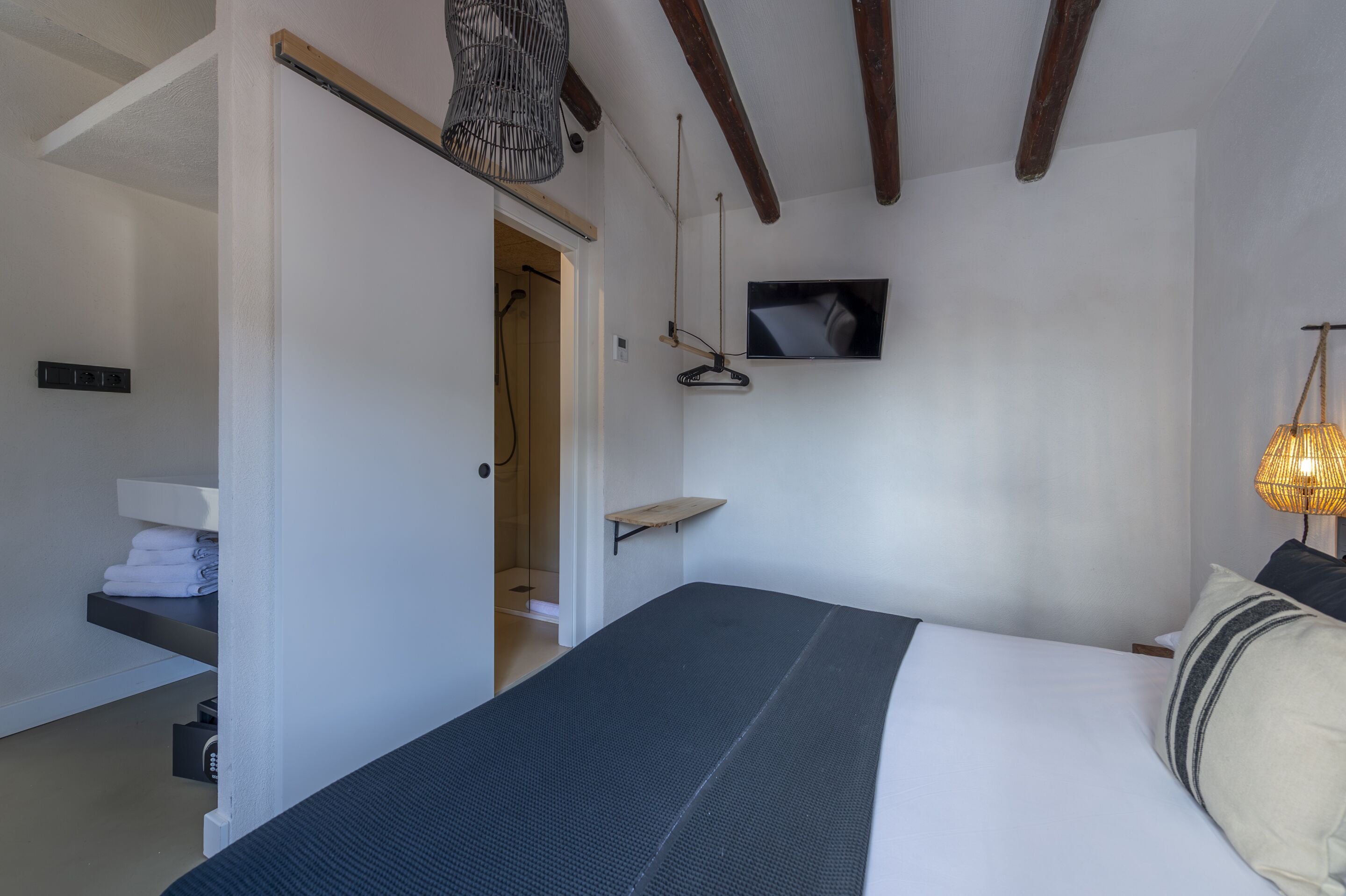 A bedroom with a bed, a TV mounted on the wall, a hanging light fixture, and a door leading to a bathroom.