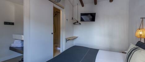 A bedroom with a bed, a TV mounted on the wall, a hanging light fixture, and a door leading to a bathroom.