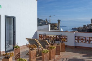 Une terrasse sur le toit, avec une table et des chaises, des plantes en pot et une vue sur la mer et les bâtiments.