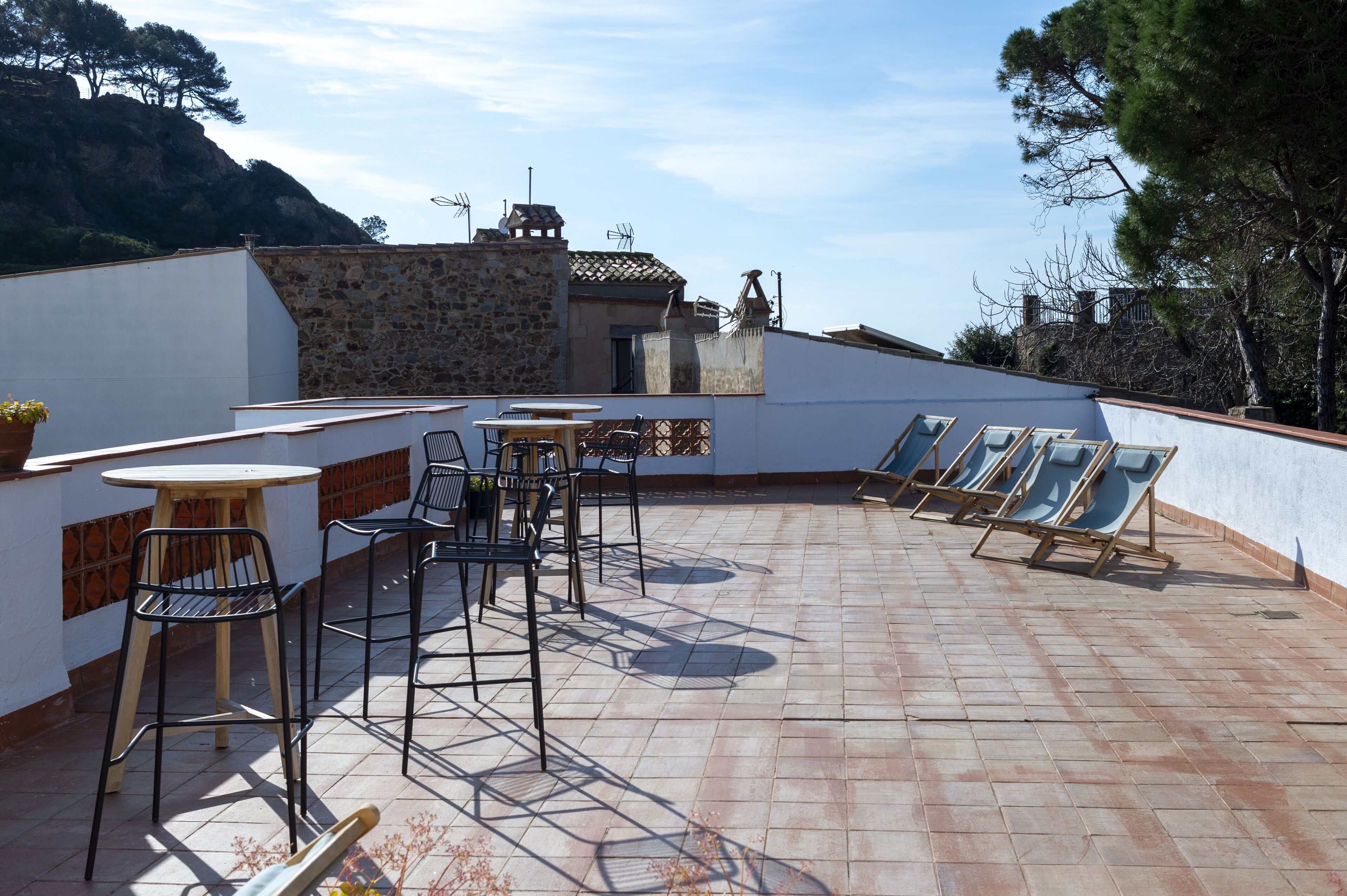 An outdoor patio with a table and chairs, a sun lounger area, and a stone building in the background.