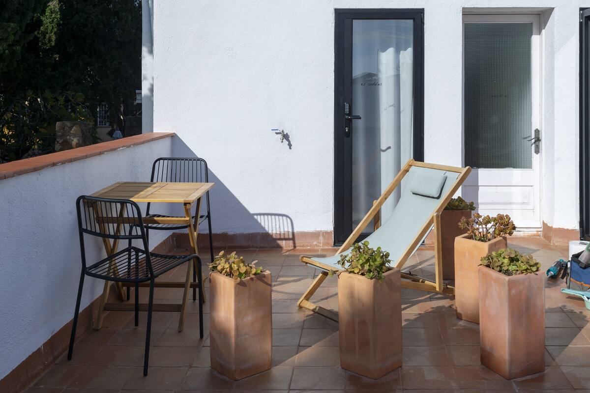 A patio with a table and chairs, a sun lounger, and potted plants.