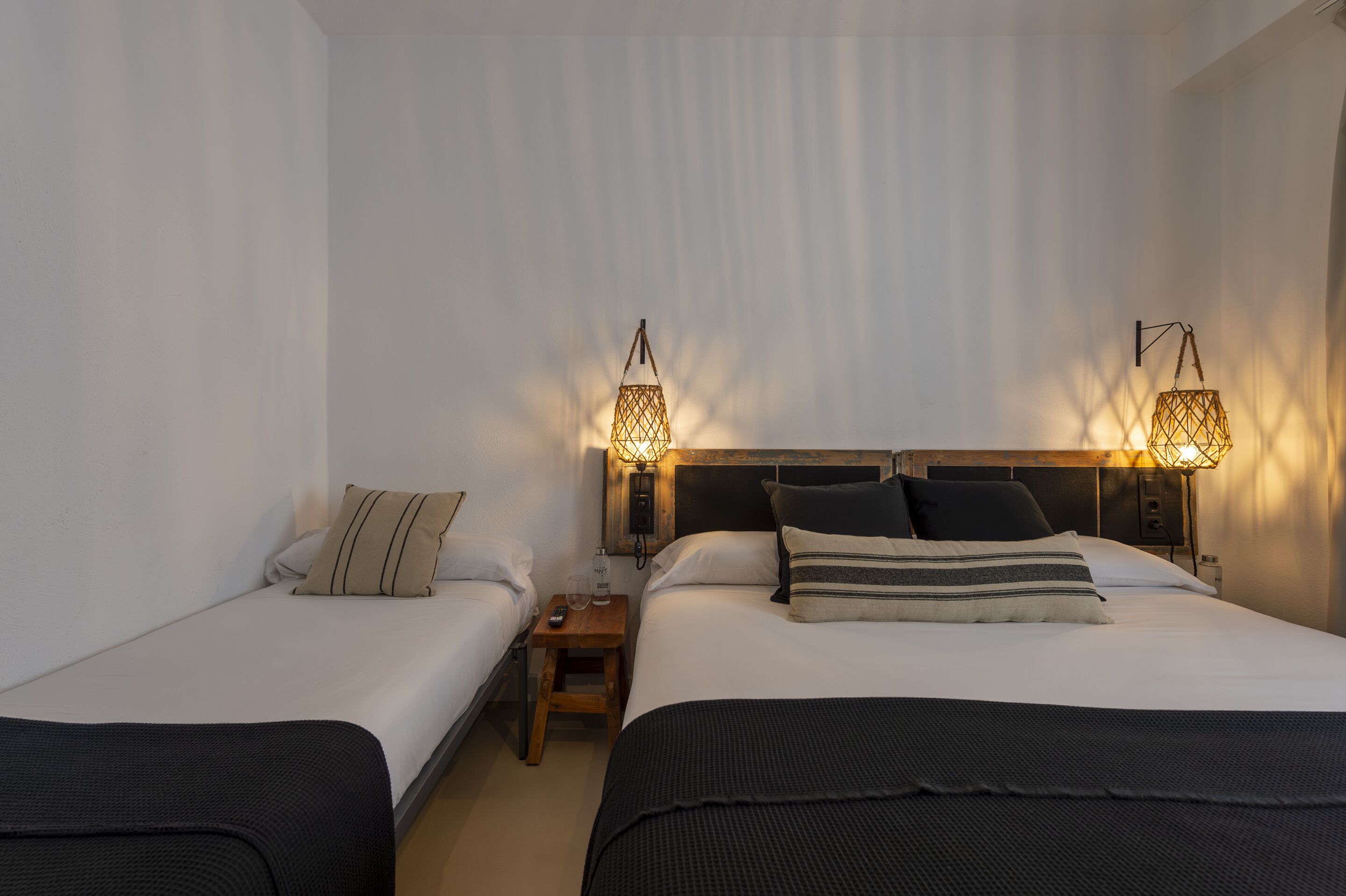 Habitación de hotel con dos camas individuales, una mesita de noche con lámpara y cabecero de madera.