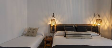 Habitación de hotel con dos camas individuales, una mesita de noche con lámpara y cabecero de madera.
