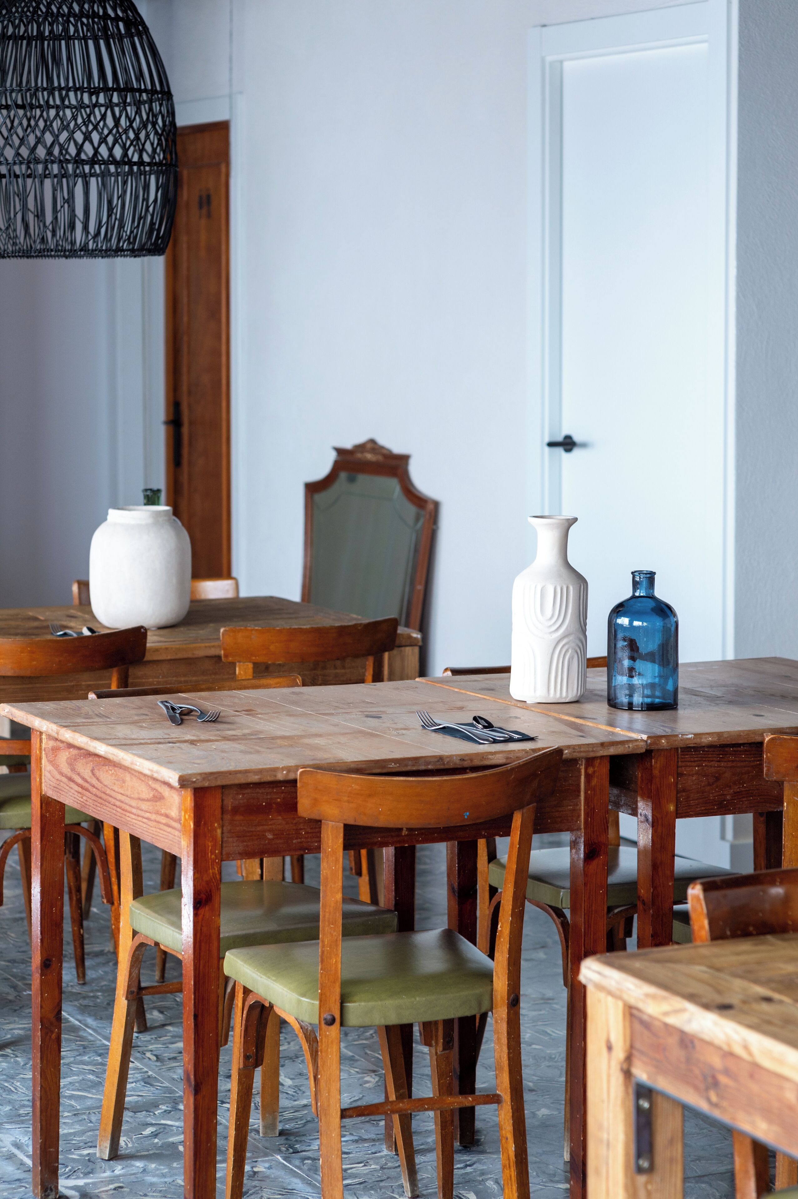 A dining area with wooden tables and chairs, a white vase, and a blue bottle on the table.