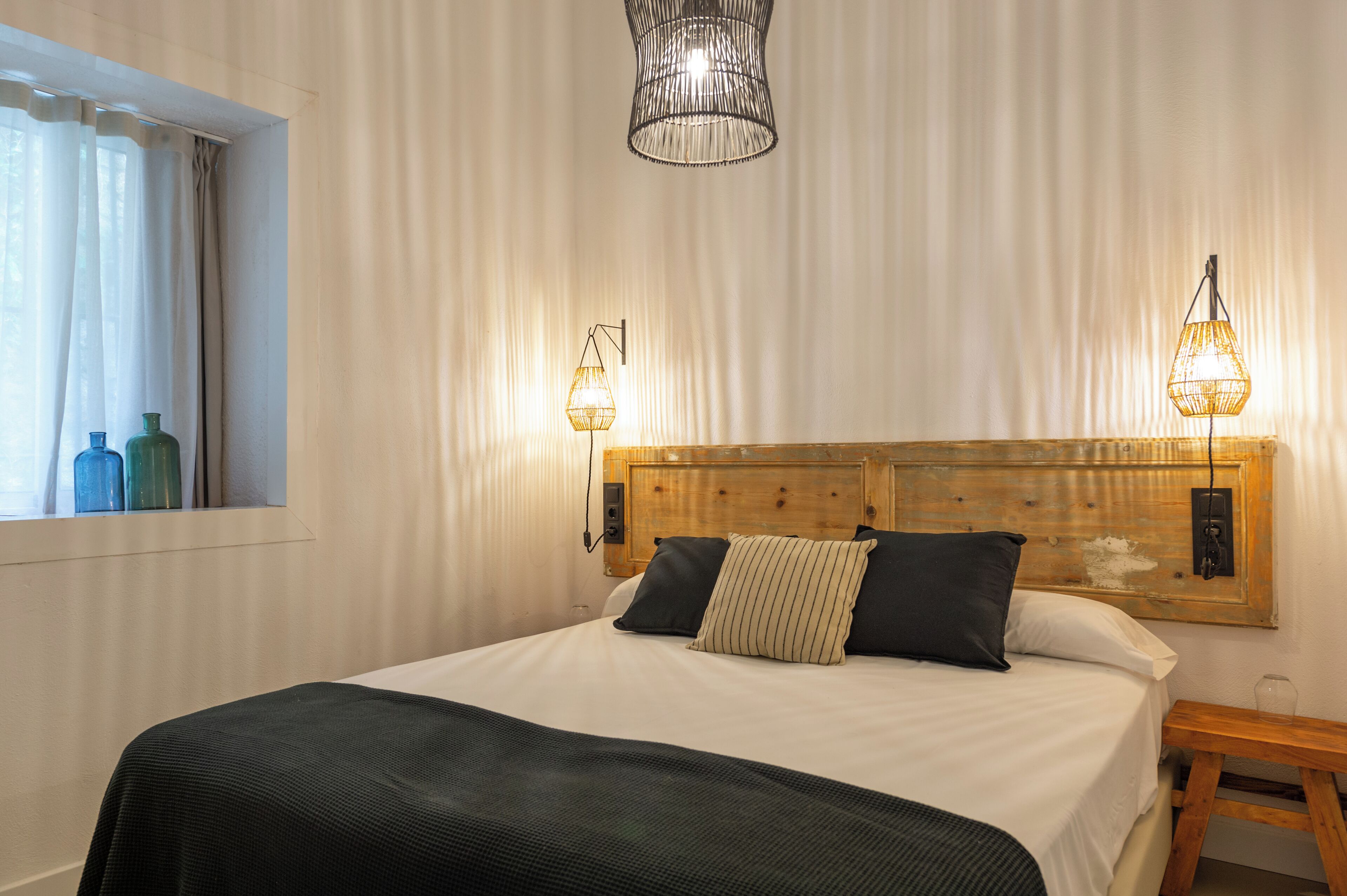 A neatly made bed with a wooden headboard, two bedside lamps, and a window with curtains.