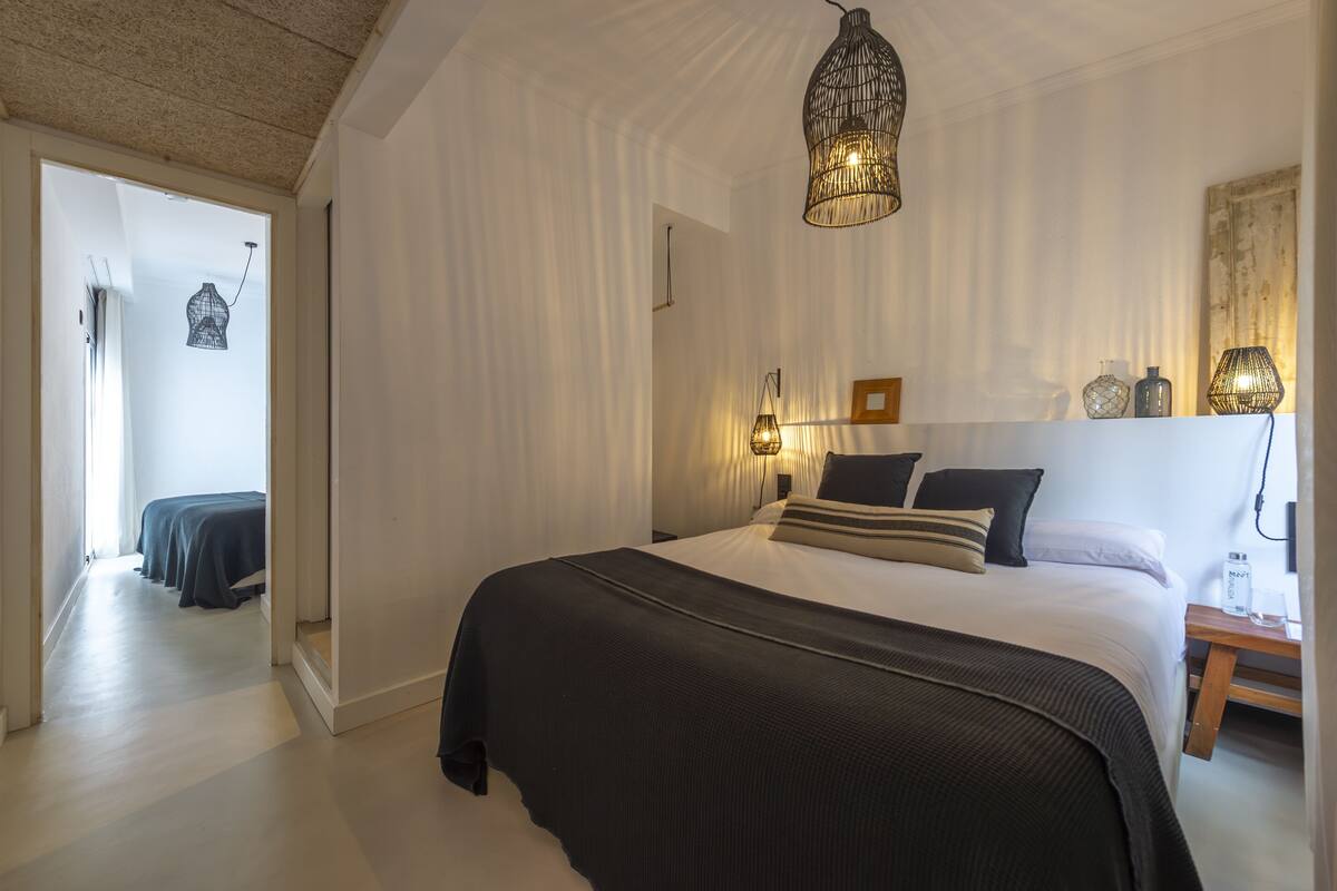 A bedroom with a large bed, a hanging light fixture, and a bedside table with a lamp.