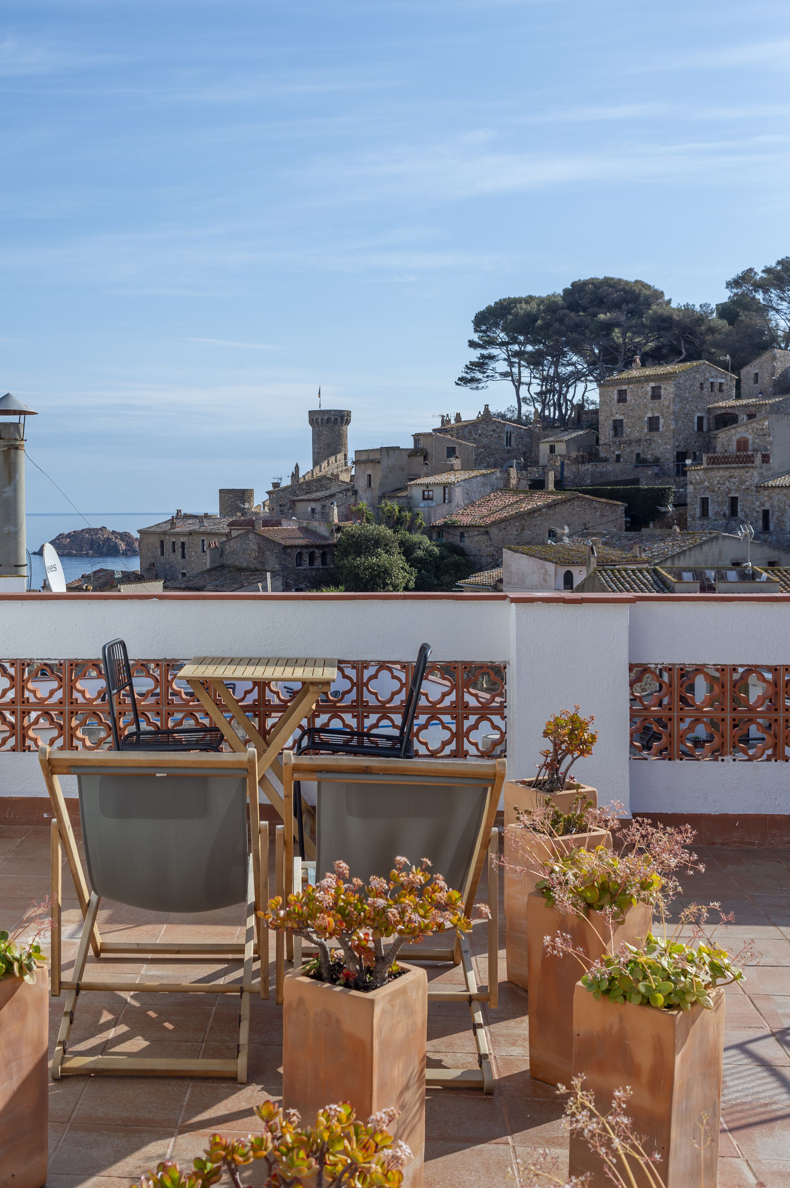 Una terrazza con posti a sedere all'aperto e piante in vaso, affacciata su un villaggio costiero con edifici storici.
