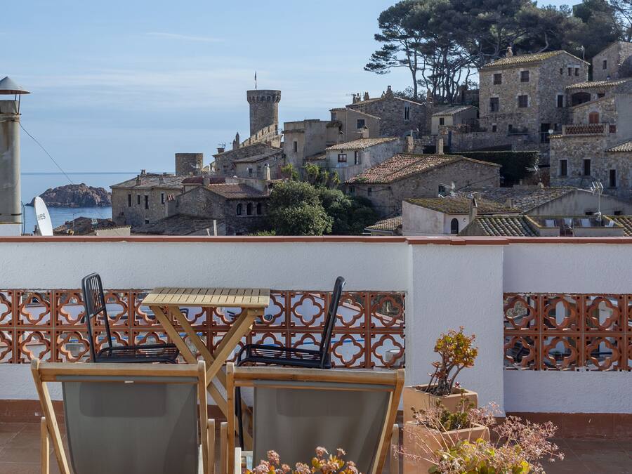 Una terrazza con posti a sedere all'aperto e piante in vaso, affacciata su un villaggio costiero con edifici storici.