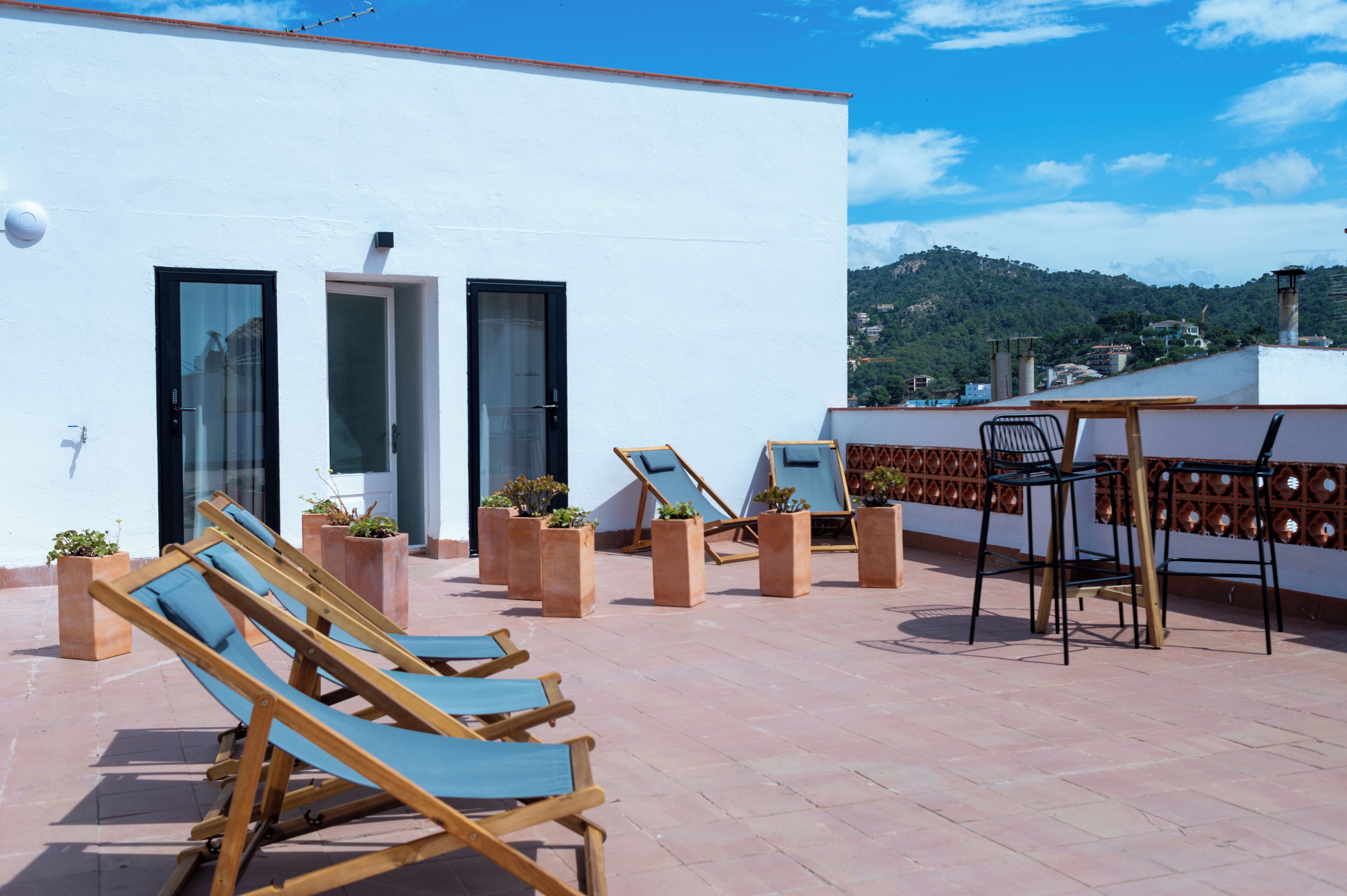 A rooftop terrace with sun loungers, a table, and potted plants.