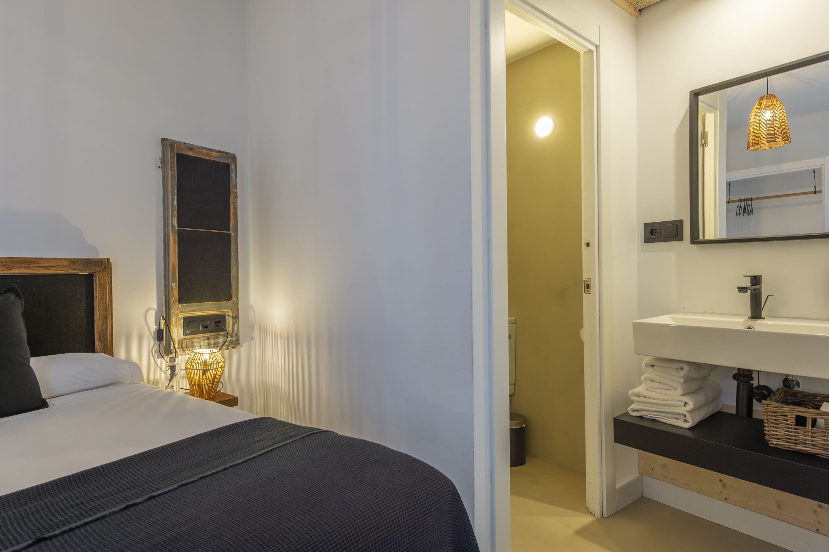 A bedroom with a bed, bedside lamp, and a mirror above a sink.
