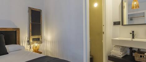 Un dormitorio con cama, lámpara de noche y espejo sobre un lavabo.