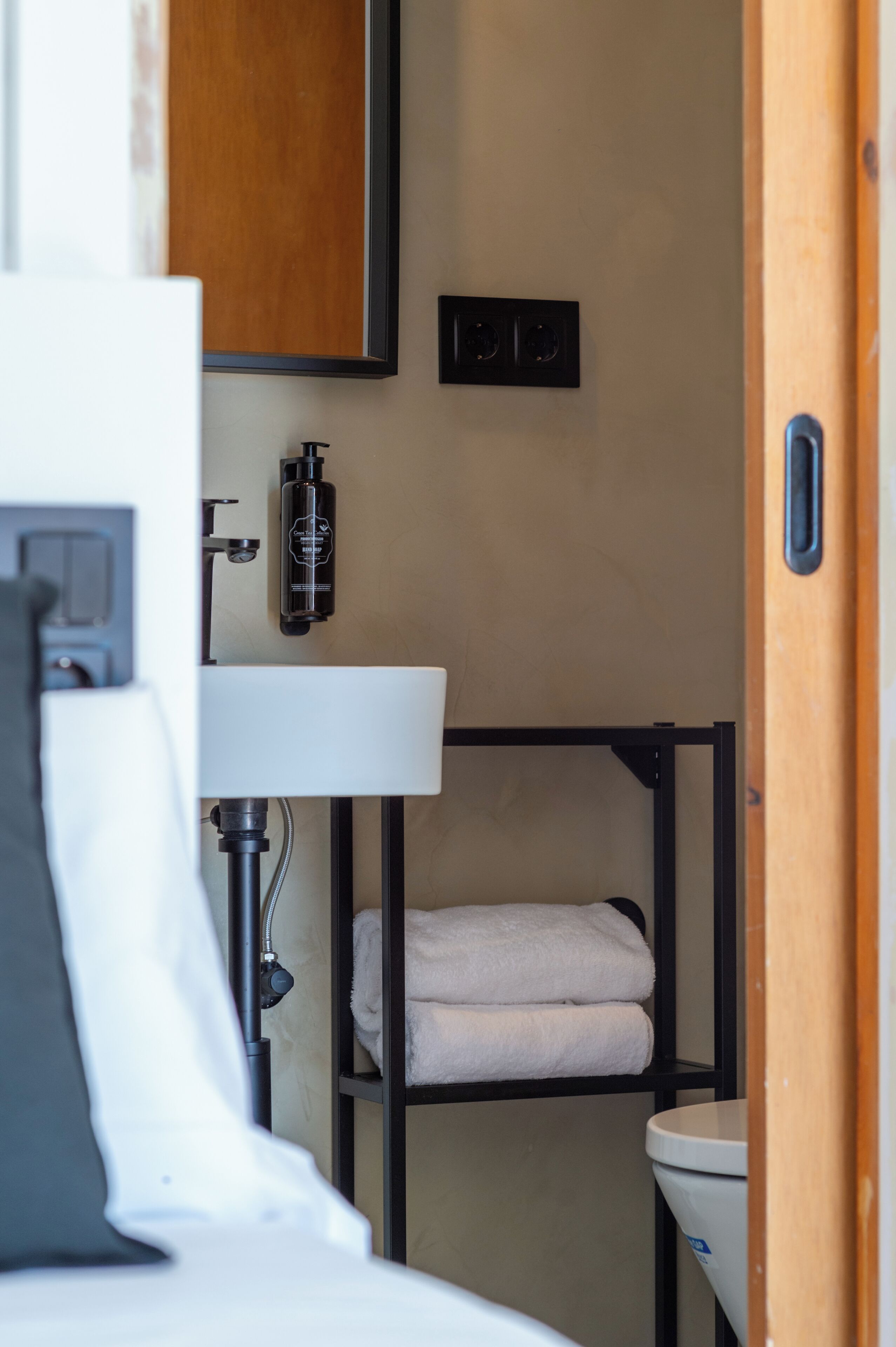 A compact bathroom with a white sink, a black towel rack, and a wooden door.
