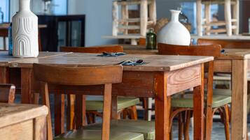 A dining area with wooden tables and chairs, a hanging light fixture, and shelves with various decorative items.
