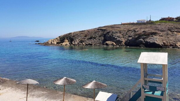 A beach with clear blue water, rocky cliffs, and a lifeguard tower.