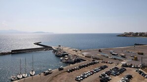 A marina with boats docked, a parking area, and a view of the sea and distant land.