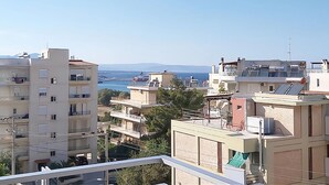A residential area with multi-story buildings, balconies, and a clear view of the sea and distant mountains.