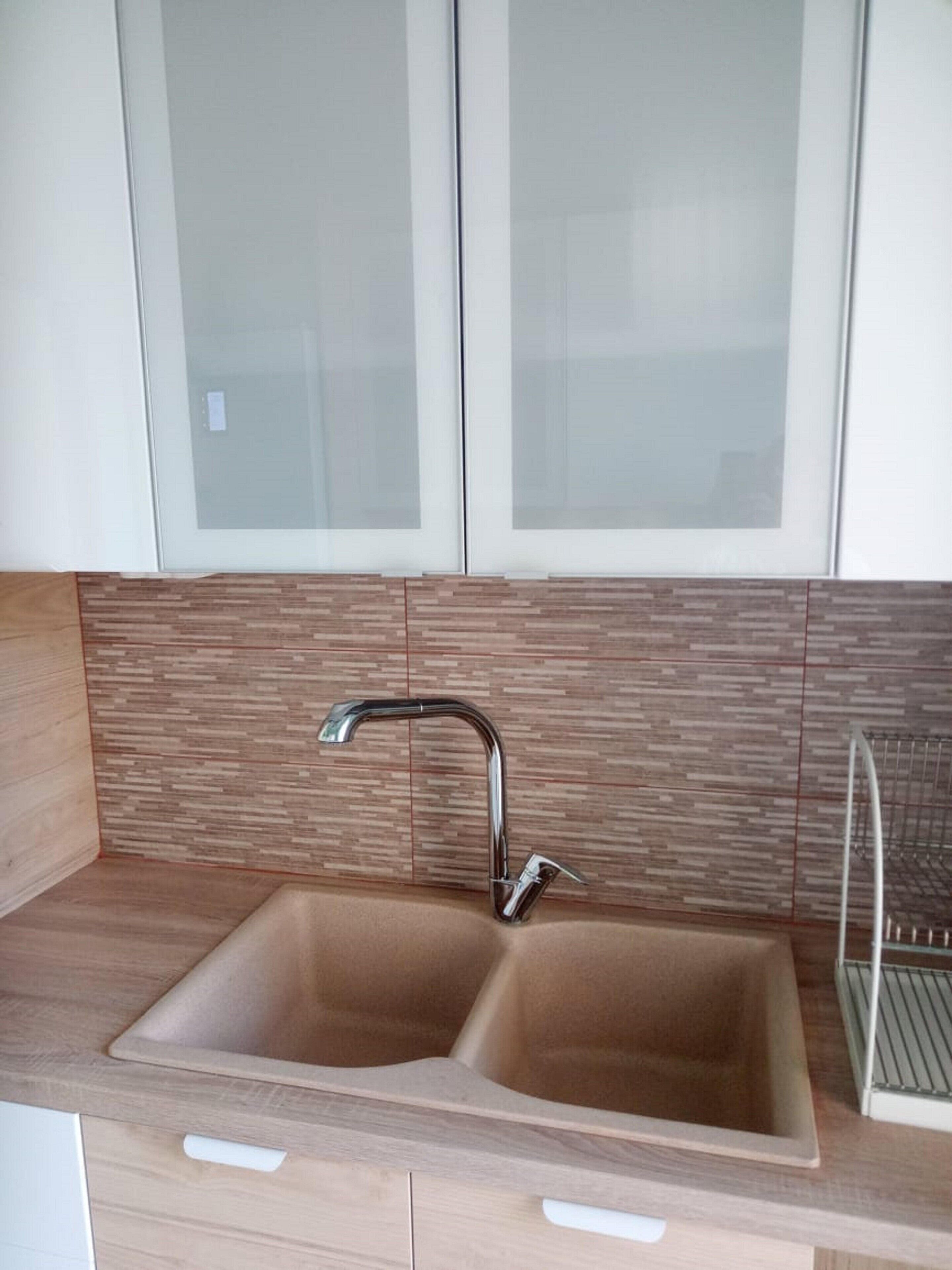 A kitchen with a double sink, wooden countertop, and a backsplash with a wood-like pattern.