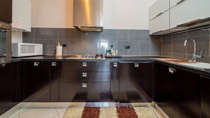 Una cocina moderna con armarios oscuros, una campana extractora de acero inoxidable, un microondas y un lavamanos.