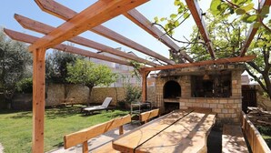 An outdoor patio with a stone barbecue area, wooden benches, and a pergola structure.