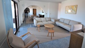 A spacious living area with a sofa set, a coffee table, and a dining table. An archway leads to a kitchen and dining area.