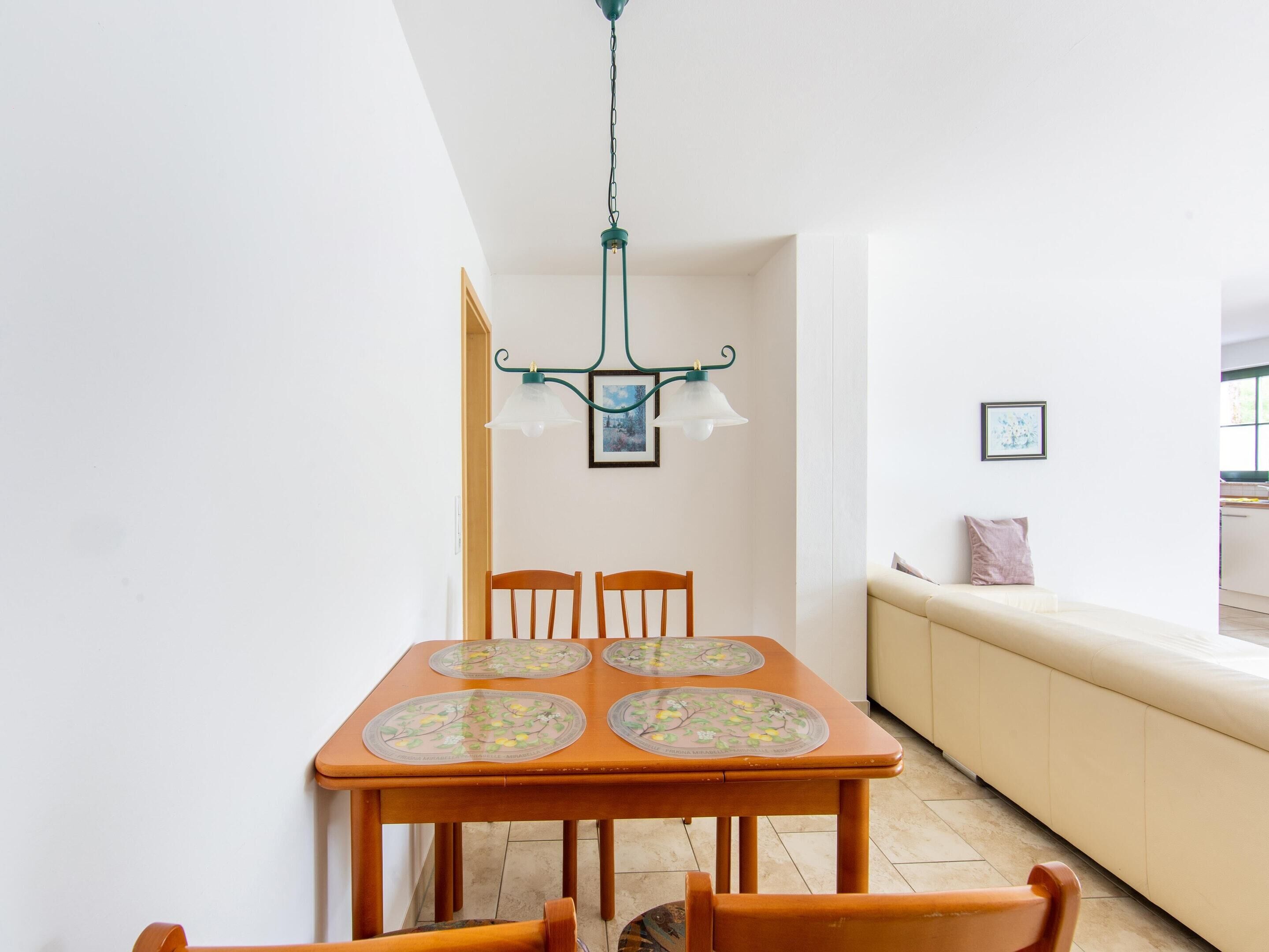 Ein Essbereich mit Holztisch und Stühlen, einer Hängelampe und einer Couch an der Wand.