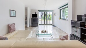 Un salon moderne avec un canapé, une table basse en verre, un téléviseur et une cuisine en arrière-plan.