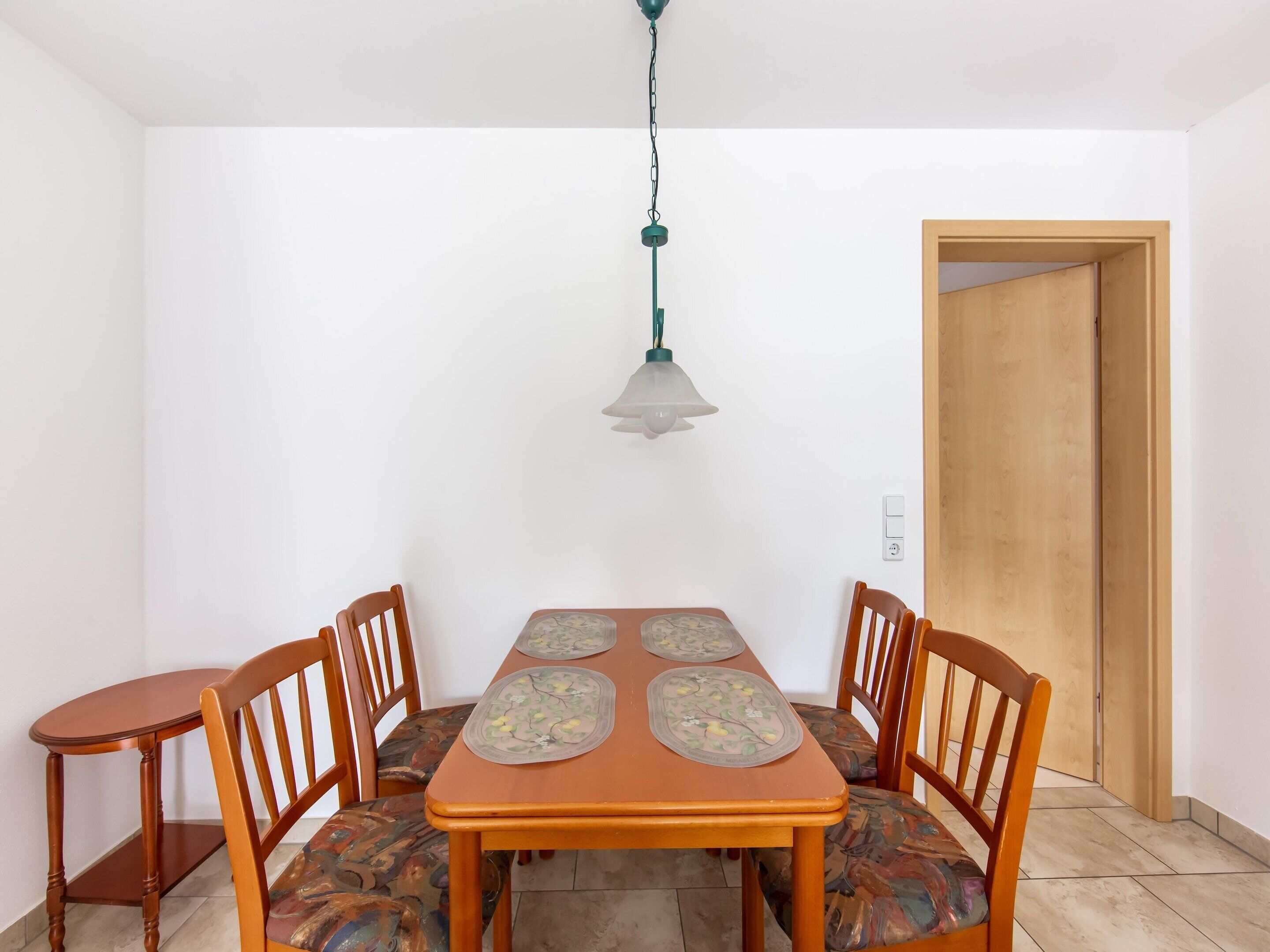 Un comedor con una mesa de madera y cuatro sillas, una lámpara colgante y una puerta de madera.