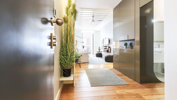 A modern hallway with wooden flooring, a potted plant, a ceiling fan, and a kitchen area with a sink and cabinets. - Modern Chiado by Homing (Lisbon)