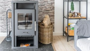 A modern living room with a stone wall, a grey fireplace, a wicker basket, and a shelf with decorative items. - Ferienhaus in Suhl in der Nahe des Rennsteigs (Suhl)