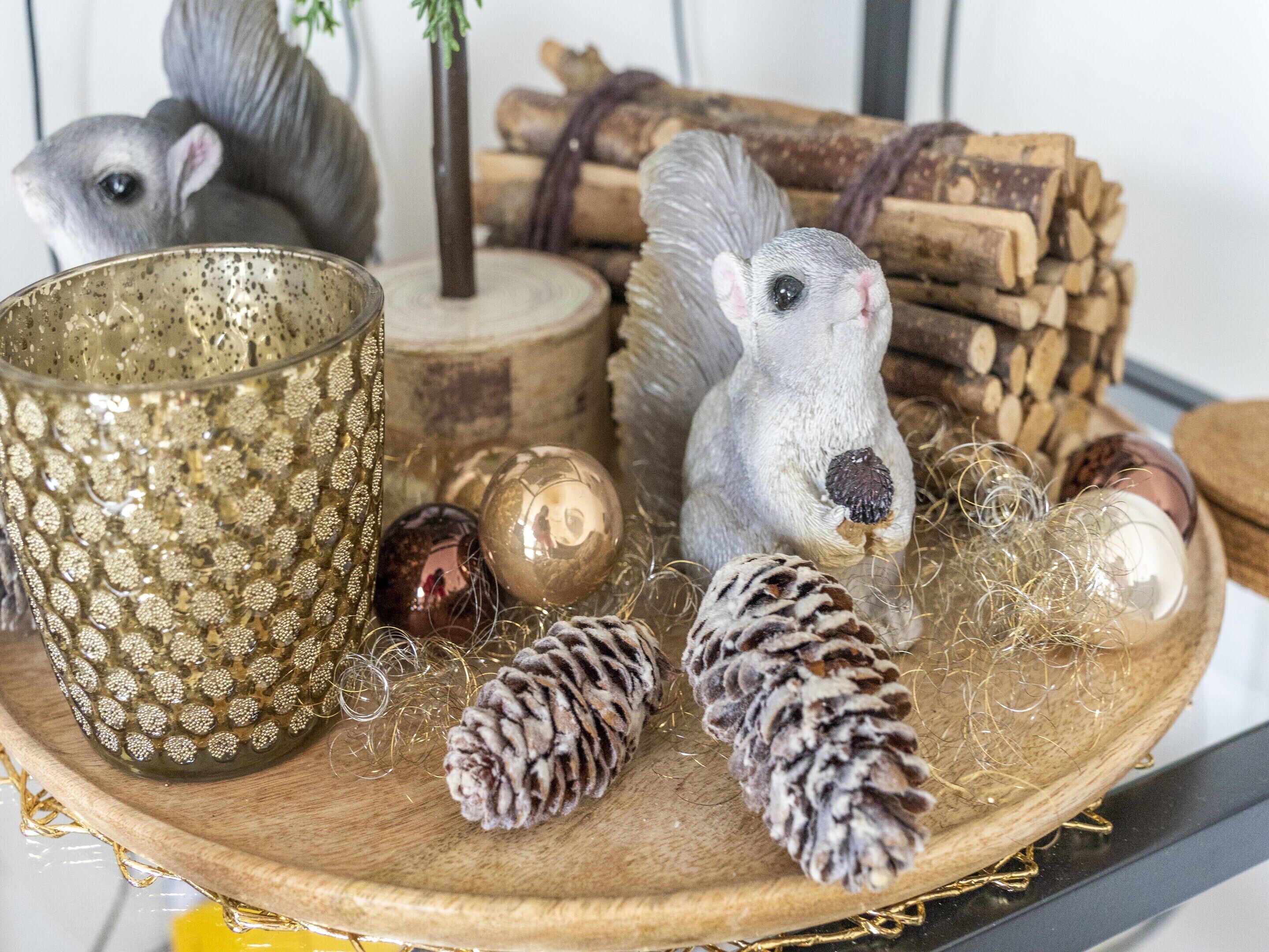 A wooden tray with decorative items including a glass, pinecones, and figurines.