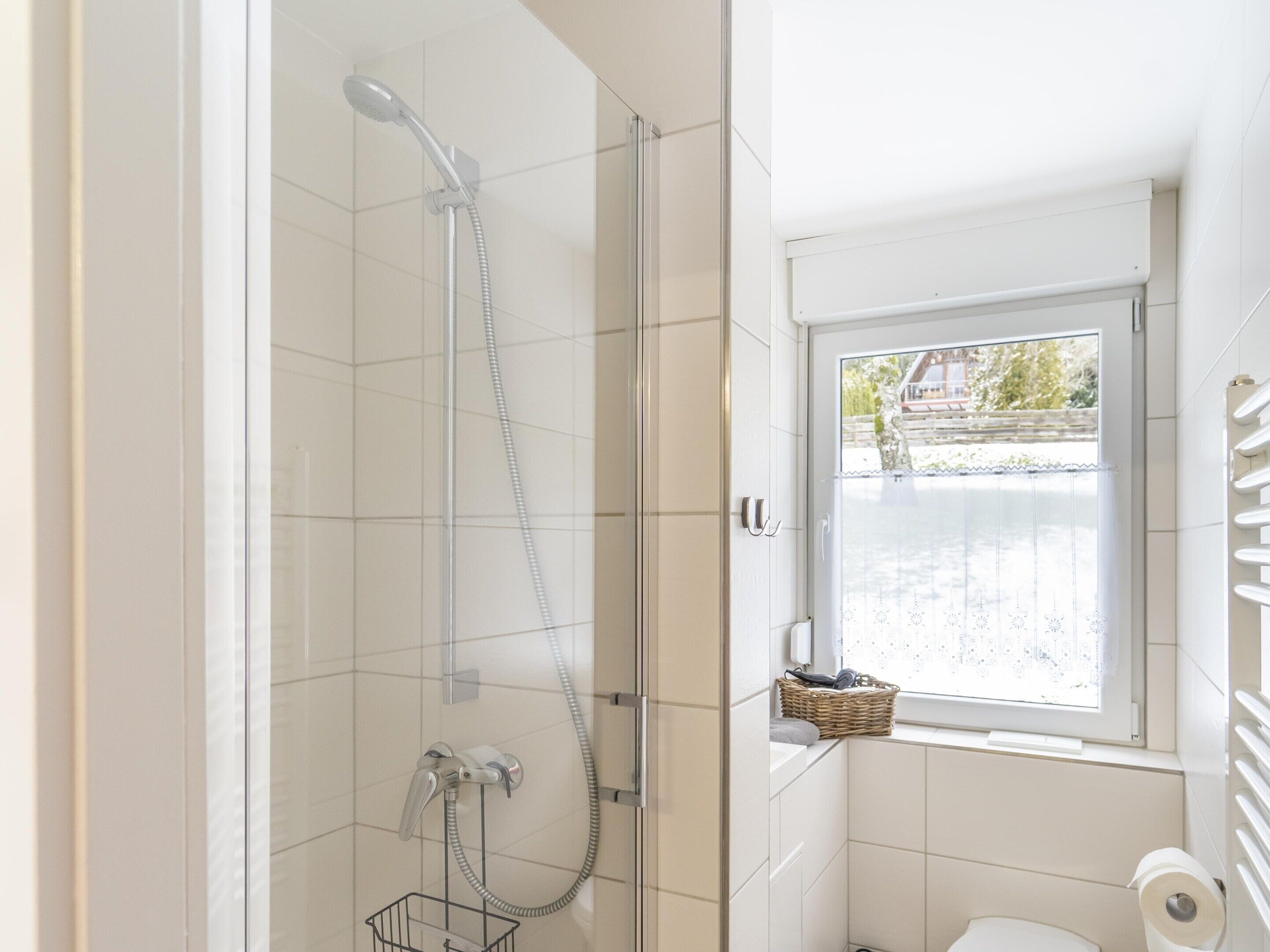 Une salle de bain équipée d’une douche, de toilettes et d’une fenêtre donnant sur l’extérieur.