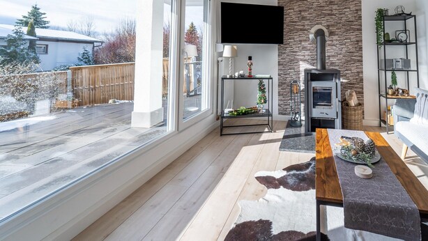A modern living room with a fireplace, a flat-screen TV mounted on the wall, and a large window overlooking a backyard. - Ferienhaus in Suhl in der Nahe des Rennsteigs (Suhl)