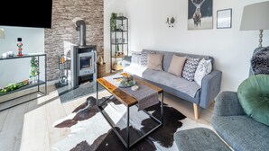 A modern living room with a stone wall, a fireplace, a sofa, a coffee table, and a green armchair. - Ferienhaus in Suhl in der Nahe des Rennsteigs (Suhl)